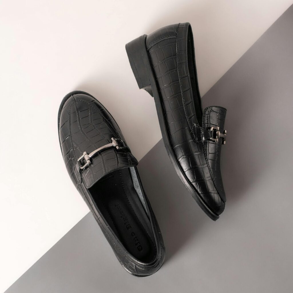 Sophisticated black leather loafers placed on a gray and white background, showcasing texture and design.